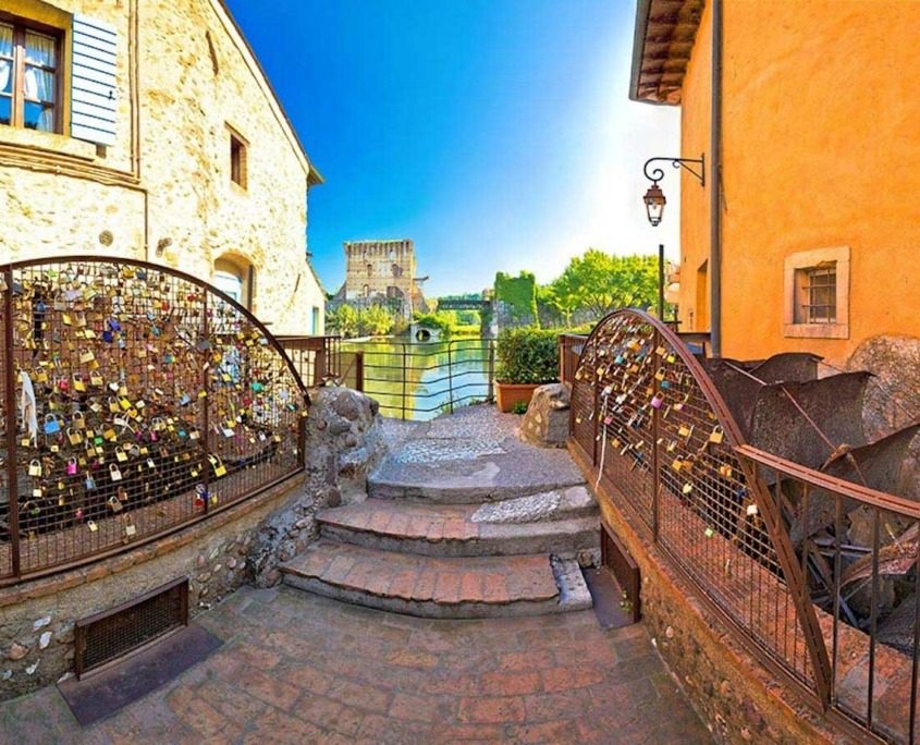 Historic water mills and stone bridge in Borghetto sul Mincio, Italy, with the Mincio River flowing gently beneath, surrounded by lush greenery.