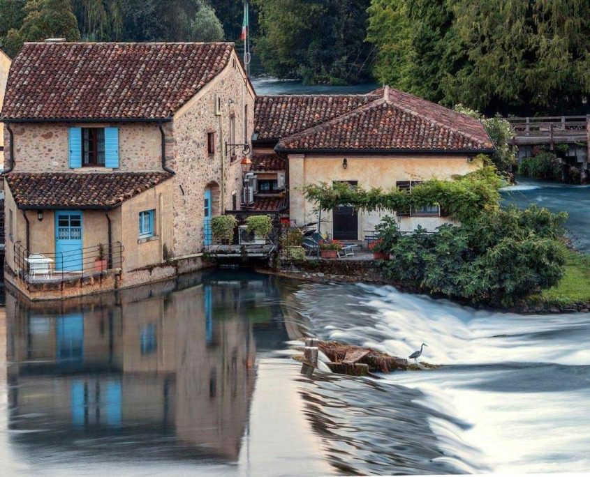 Picturesque village scene in Borghetto sul Mincio, with small stone houses featuring terracotta roofs and colorful shutters lining the riverbanks.