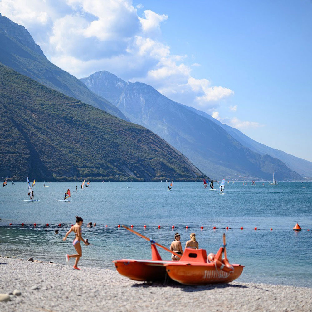 View of Torbole Beach with girls playing and windsurfers in the background.