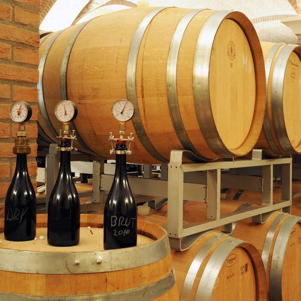 Wooden barrels with wine and a few bottles of classic method sparkling wine.