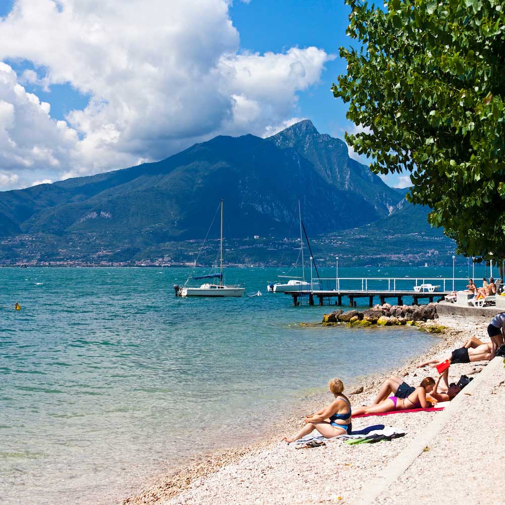 People relaxing on a pebbled beach in Torri del Benaco, Lake Garda.