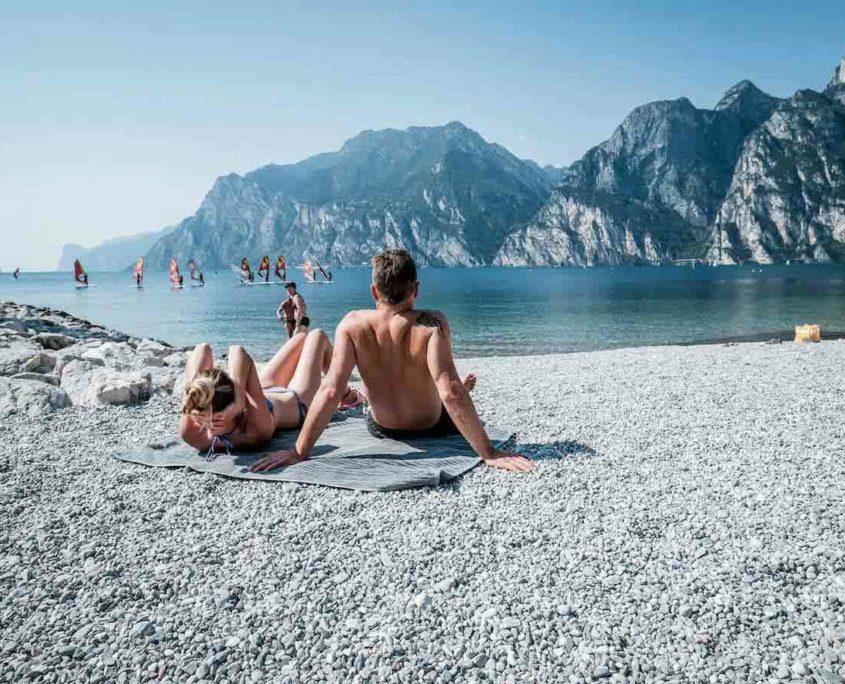 People relaxing and watching windsurfers in the beach of Torbole, Lake Garda.