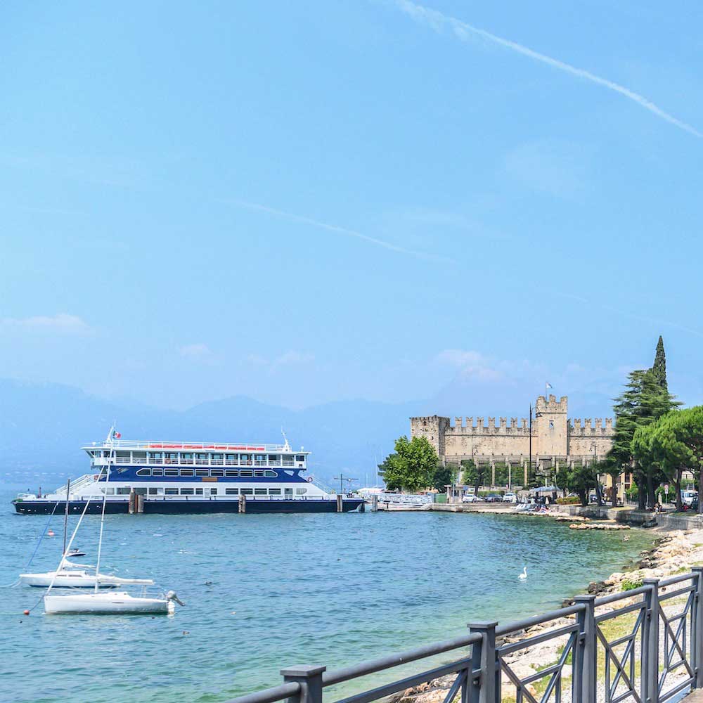 View of the Torri del Benaco pier with the car ferry departing and crossing Lake Garda.